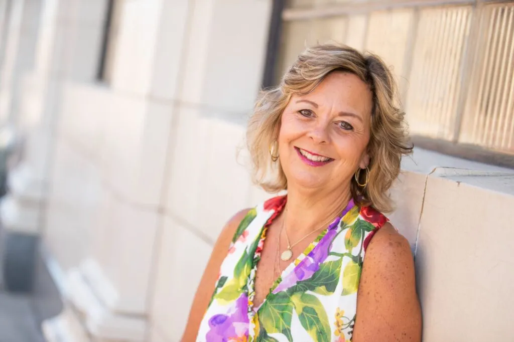 Smiling middle-aged woman in floral dress, showcasing confidence and a radiant smile, representing the positive outcomes of orthodontic treatments like Invisalign at VanLaecken Orthodontics.