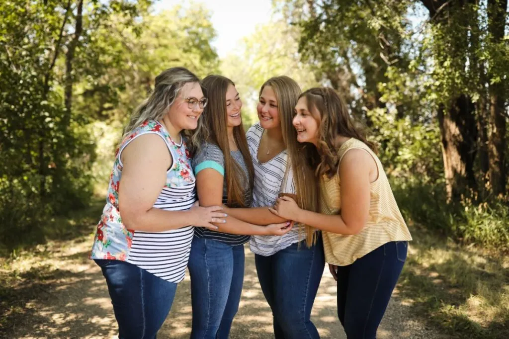 Group of four young women smiling and enjoying each other's company outdoors, surrounded by trees, illustrating friendship and positivity.